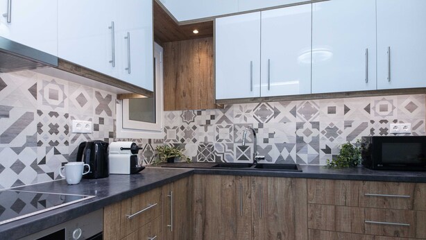 A modern kitchen with wooden cabinets, a black countertop, and a patterned backsplash. - Boutique Stylish 1 Bd Apt in Patisia (Athens)
