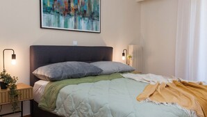 A modern bedroom with a bed, bedside tables, a cityscape painting, and a ceiling light. - Boutique Stylish 1 Bd Apt in Patisia (Athens)