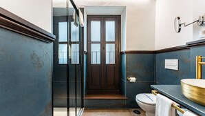 Un baño con cabina de ducha de vidrio, inodoro y lavamanos con grifo dorado.