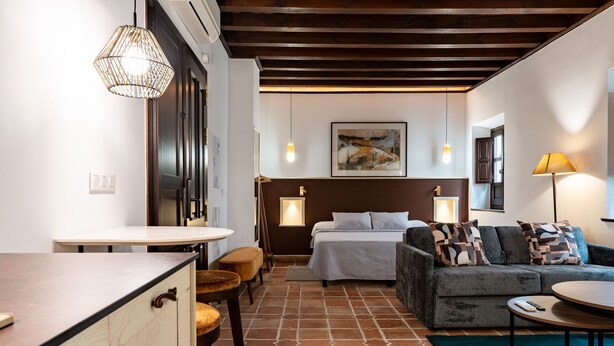 Una habitación de hotel moderna con cama, sofá, mesa de comedor y zona de cocina.