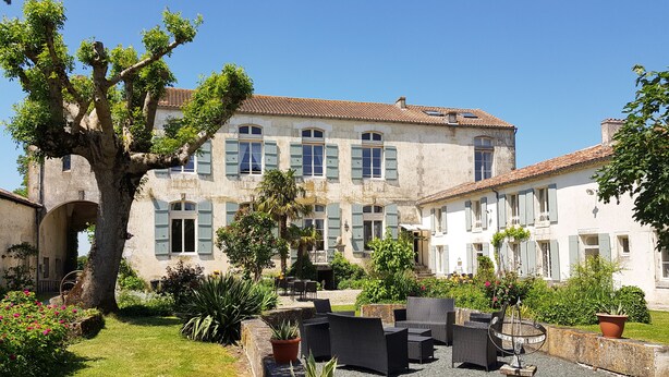 A courtyard with outdoor seating, a large tree, and a historic building with multiple windows and shutters. - Cottage (sleeps 4) at Domaine de Chantageasse, a 17th century estate with pool (Asnières-la-Giraud)