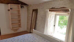 A bedroom with a wooden bed, a built-in wardrobe, a large mirror, and a window with a view of greenery. - Cottage (sleeps 4) at Domaine de Chantageasse, a 17th century estate with pool (Asnières-la-Giraud)