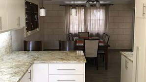 Une cuisine moderne avec des meubles blancs, des plans de travail en granit et des luminaires suspendus.