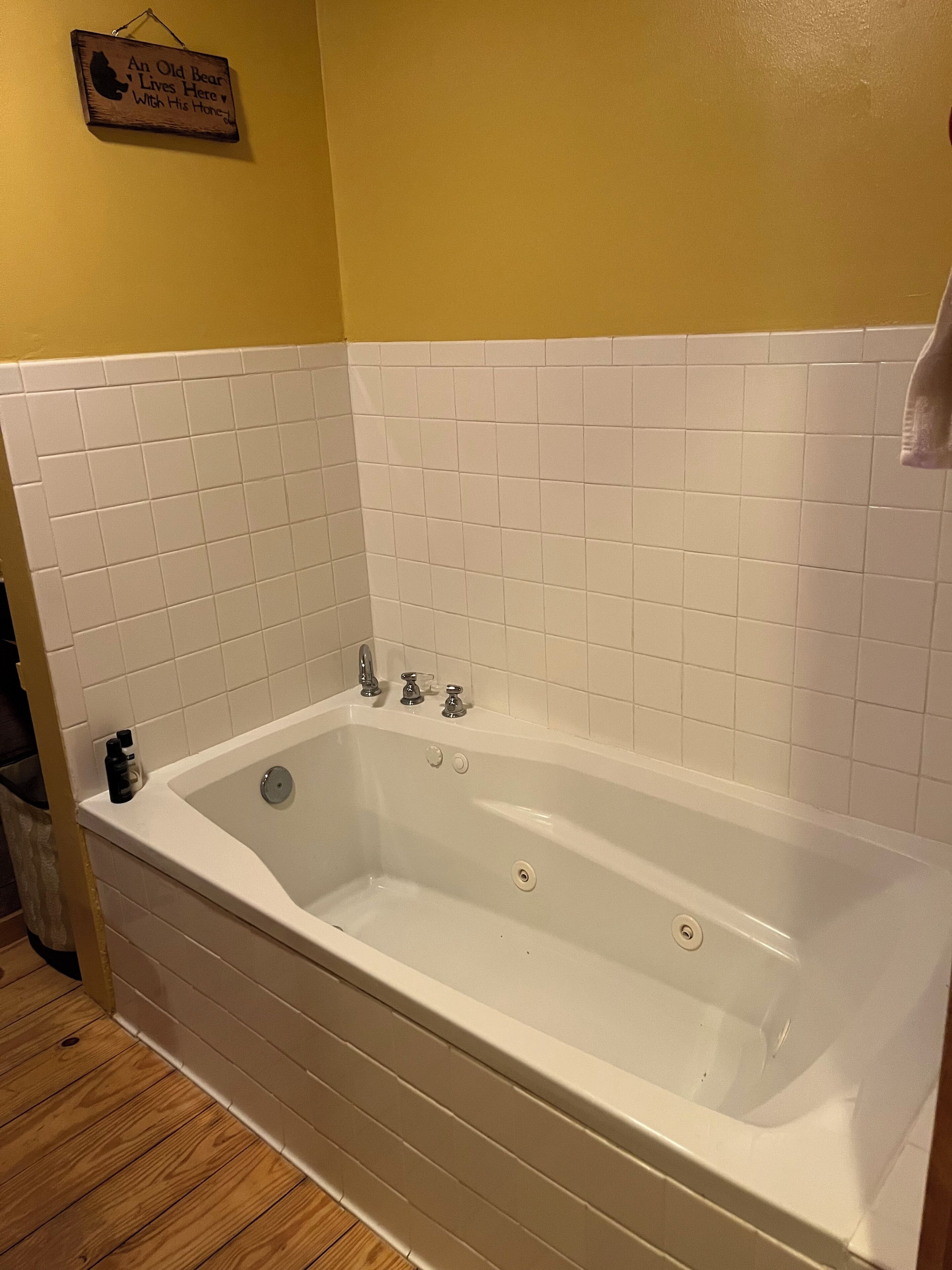 Une salle de bain avec une baignoire blanche, des murs recouverts de carreaux blancs et un plancher en bois.