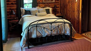 Dormitorio de cabaña de madera con cama, ventilador de techo, unidad de aire acondicionado y decoración rústica.