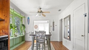 A dining area with a wooden table and chairs, a ceiling fan, and a view of the adjacent room.
