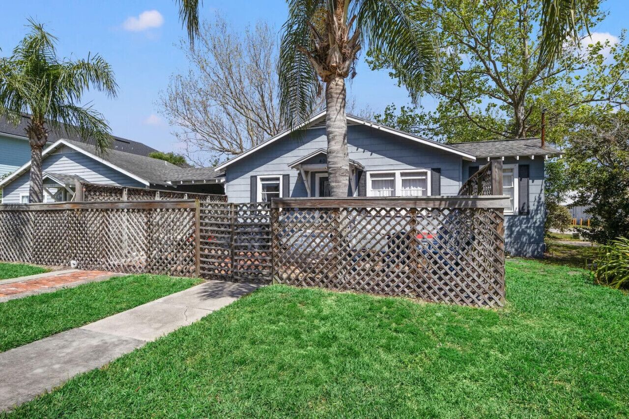 A residential house with a fenced backyard, a palm tree, and a clear sky.