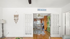A living room with a wooden floor, a dining area with a table and chairs, and a kitchen visible through an open door.