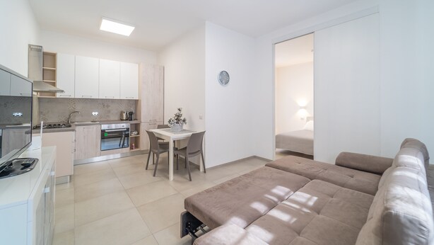 A modern apartment with a kitchenette, a dining area, a living room with a sofa, and a bedroom with a bed. - Relax Flatroom 22 (Olbia)