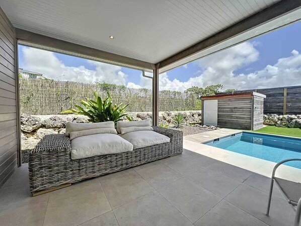 A modern outdoor living area with a wicker sofa, a pool, and a view of the backyard.