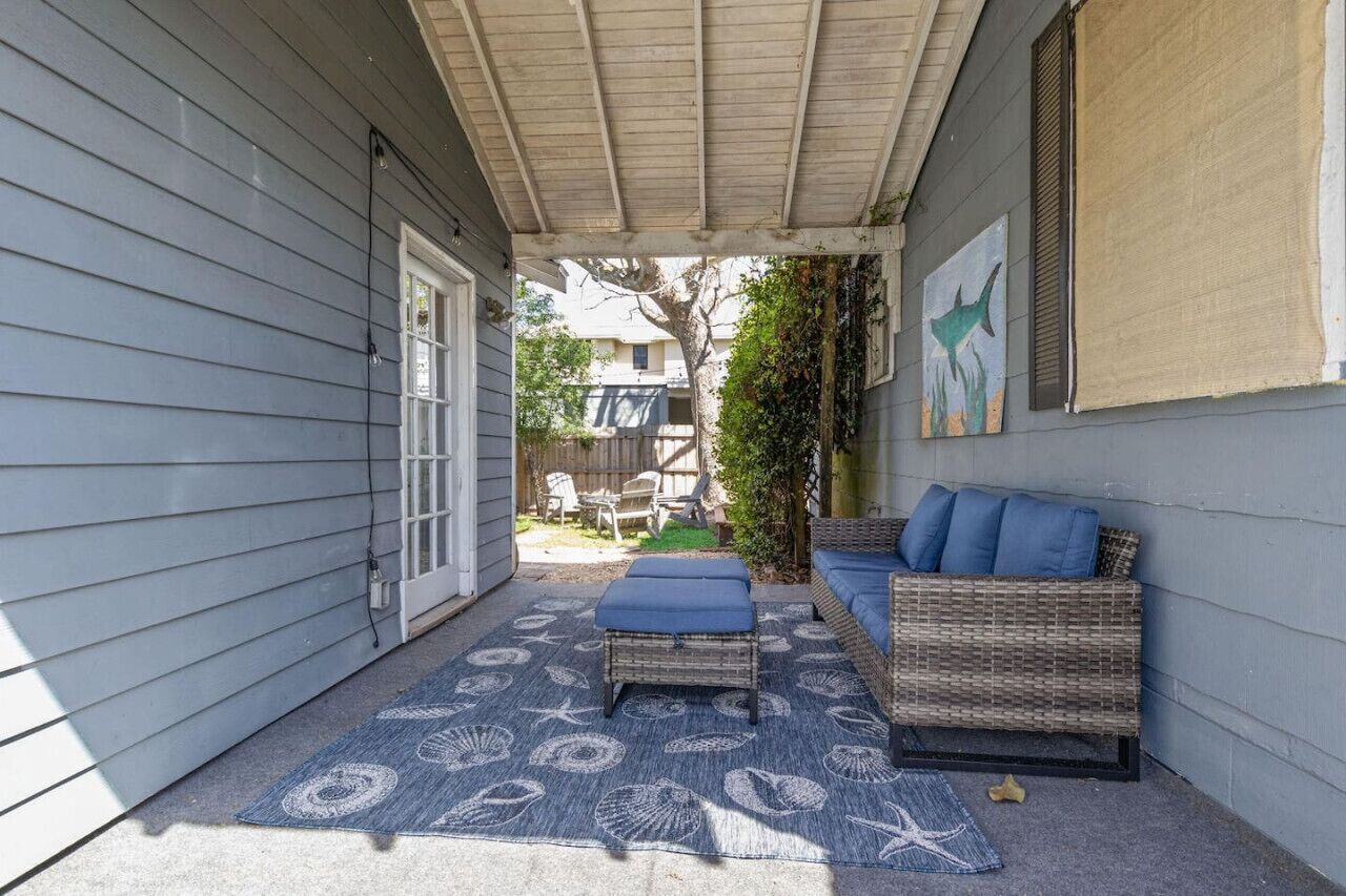 A covered patio with wicker furniture and a blue patterned rug.