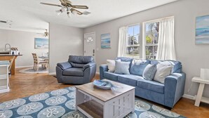 Un salon avec un canapé bleu, un fauteuil gris, une table basse en bois et un ventilateur de plafond.