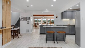 Una cucina moderna con mobili grigi, un'isola centrale con sgabelli e una scala che conduce a una sala da pranzo con vista.