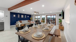 Un'area pranzo moderna con un tavolo lungo apparecchiato per sei persone, una parete di accent blu e vista sull'esterno.