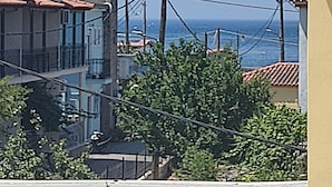 Un bâtiment situé sur la côte, doté d’un balcon, offrant une vue dégagée sur la mer et agrémenté d’un parasol bleu et rose.