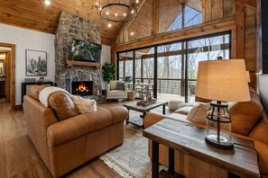 A cozy living room with a stone fireplace, leather sofas, and a large window offering a view of the outdoors. - NEW On Cloud Wine, Lux /Modern AMAZING Mtn.Views /Hot Tub/ Fire Pit/Private Deck (Blue Ridge)
