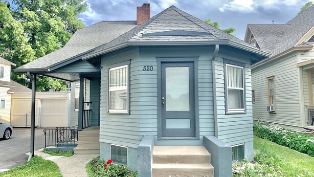 Una casa pequeña de un solo piso con fachada azul oscuro, un porche y un garaje.