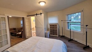 Un dormitorio con cama, vestidor, ventana con vistas y puerta que da a otra habitación.