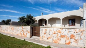 Une maison moderne avec une façade en pierre, une entrée sécurisée par un portail et un ciel d’un bleu éclatant.