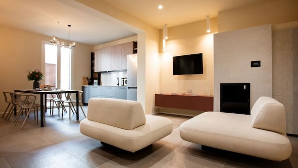 Un salon moderne avec deux canapés, un coin repas avec une table et des chaises, une cuisine équipée de meubles et un téléviseur fixé au mur.