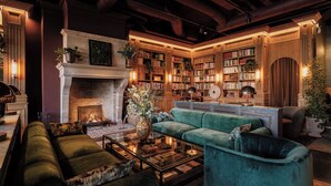 A cozy living room with a fireplace, green sofas, a coffee table, and a bookshelf filled with books. - Villa Foresta (Lidingo)