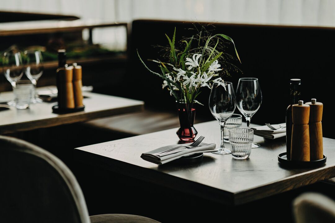 A dining table set with a vase of flowers, wine glasses, and salt and pepper shakers.