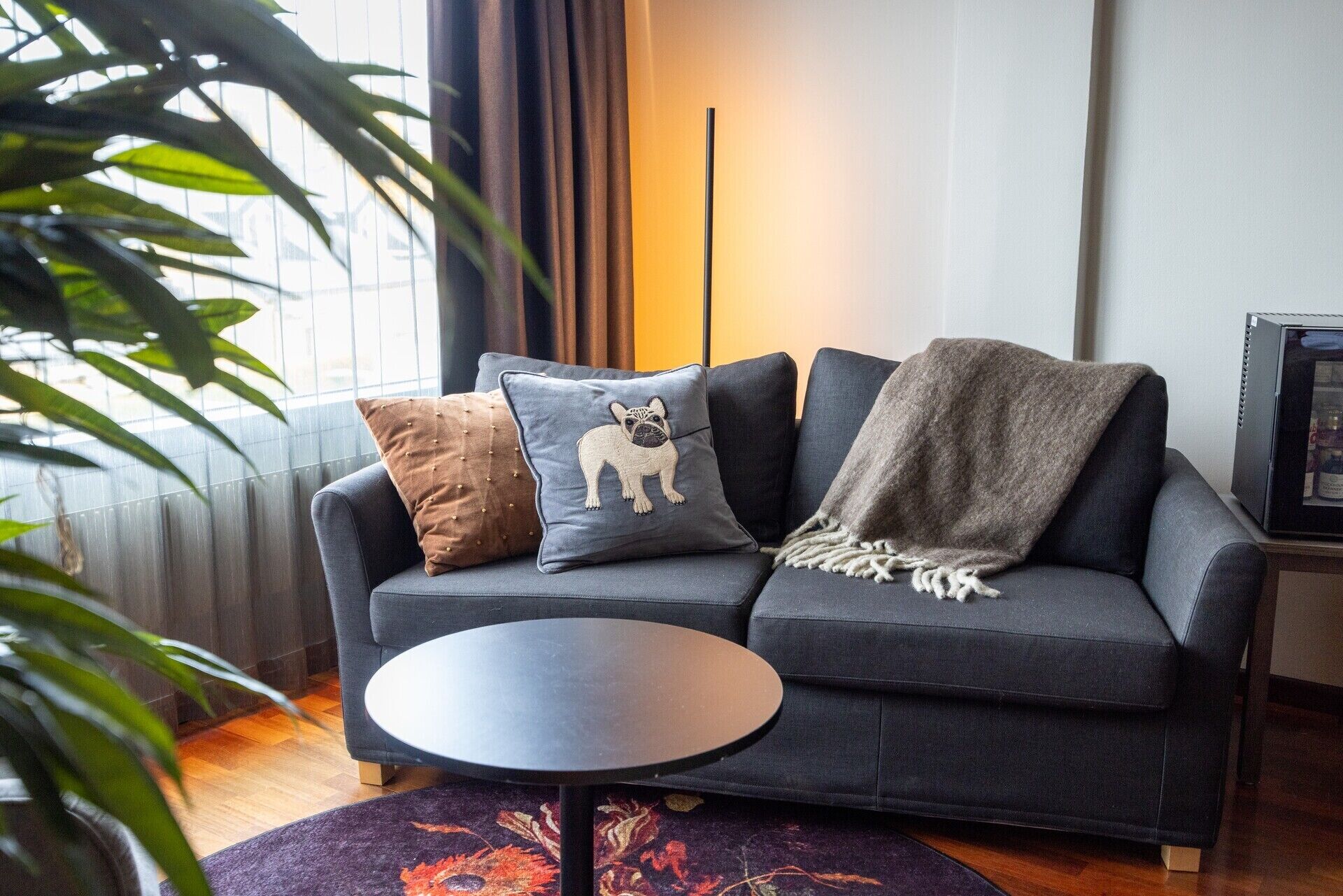 Un salon moderne avec un canapé gris foncé, deux coussins décoratifs, un plaid et une petite table ronde.