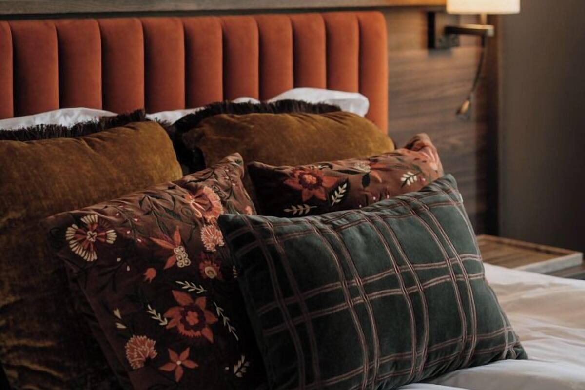 A bed with multiple pillows, a headboard, a framed artwork on the wall, and a bedside lamp.