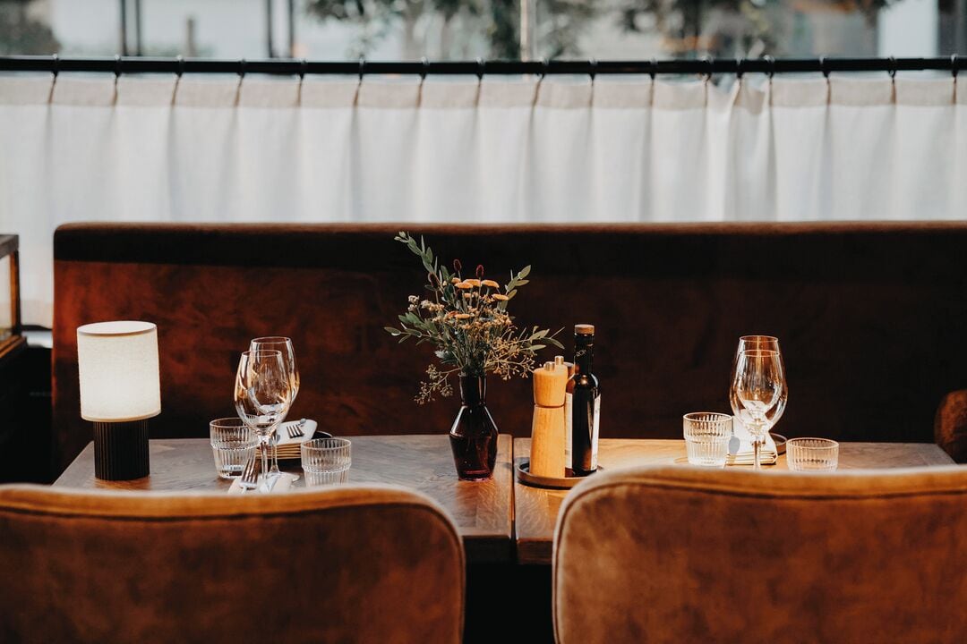 Un restaurante con una mesa de madera preparada para dos comensales, un florero con flores y una botella de aceite de oliva.