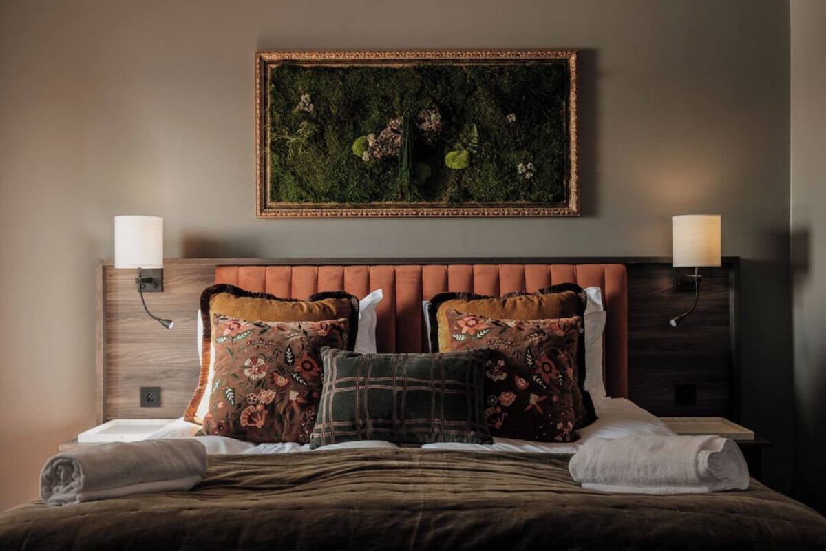 A neatly made bed with multiple pillows, a framed artwork above, and two bedside lamps.