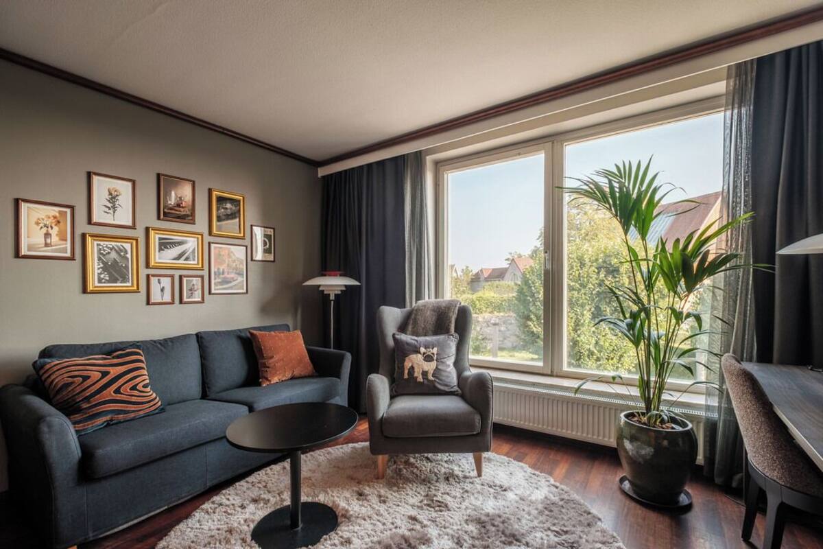 A living room with a sofa, armchair, coffee table, and a large window with a view of greenery.