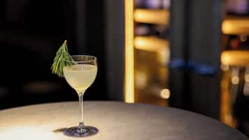 Un cocktail servi dans un verre à martini, décoré d’une branche, sur une table en marbre.