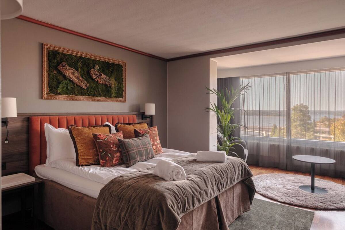 A modern hotel room with a large bed, a view of the city, and a large window.