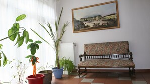 A room with a bench, potted plants, a radiator, and a framed picture on the wall. - Hotel Admiral (Vienna)