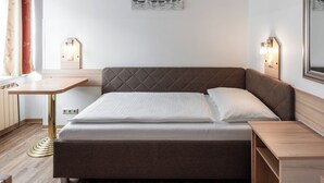 A neatly arranged hotel room with a bed, bedside tables, a desk, and a wall-mounted lamp. - Hotel Admiral (Vienna)