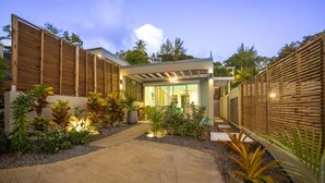 Una casa moderna con un porche cubierto, un sendero de concreto y diferentes plantas.