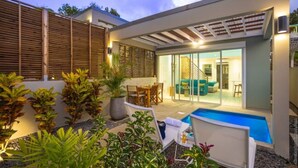 Un área de piscina moderna al aire libre con sillones reclinables, una mesa de comedor y una escalera que conduce a un nivel superior.