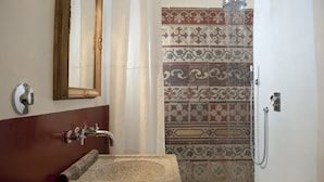 A bathroom with a stone sink, a mirror, and a shower with patterned tiles. - Casa Talia Houses (Modica)