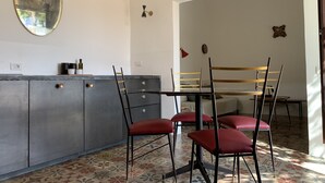 A dining area with a table and chairs, a grey cabinet with drawers, a wall-mounted mirror, and a patterned floor. - Casa Talia Houses (Modica)