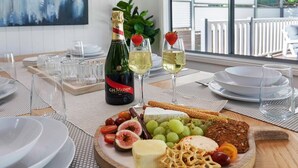 A table set for a meal with a bottle of champagne, glasses, plates, and a variety of cheeses, fruits, and crackers. - Sunset Haven 4-Bd Retreat Milton, Steps to Stadium (Petrie Terrace)
