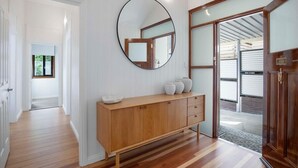A hallway with a wooden console table, a round mirror, and a door leading to a garage. - Sunset Haven 4-Bd Retreat Milton, Steps to Stadium (Petrie Terrace)