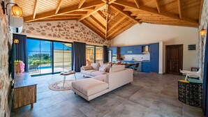 A spacious living area with a stone wall, a wooden ceiling, and a large window offering a view of the outdoors. - Kaşın en gözdesi taş villalar  (kas)