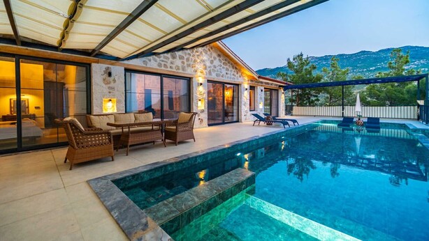 A poolside area with a stone house, outdoor seating, and a view of the sea. - Kaşın en gözdesi taş villalar  (kas)