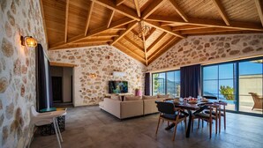 A spacious living area with a stone wall, wooden ceiling, and a large window offering a view of the outdoors. - Kaşın en gözdesi taş villalar  (kas)