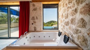 A stone-walled room with a large bathtub, a red curtain, and a window overlooking a scenic landscape. - Kaşın en gözdesi taş villalar  (kas)
