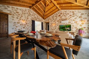 A rustic dining area with a stone wall, wooden ceiling beams, and a large wooden table set for six. - Kaşın en gözdesi taş villalar  (kas)