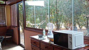 Cozinha com bancada de madeira, micro-ondas, liquidificador e janela com vista para área verde.