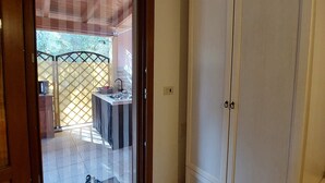 Quarto com porta de vidro deslizante para uma varanda, guarda-roupa branco e chão ladrilhado.