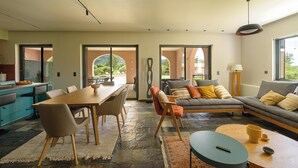 Ein modernes Wohnzimmer mit Essbereich, Steinböden und großen Fenstern mit Blick ins Freie.