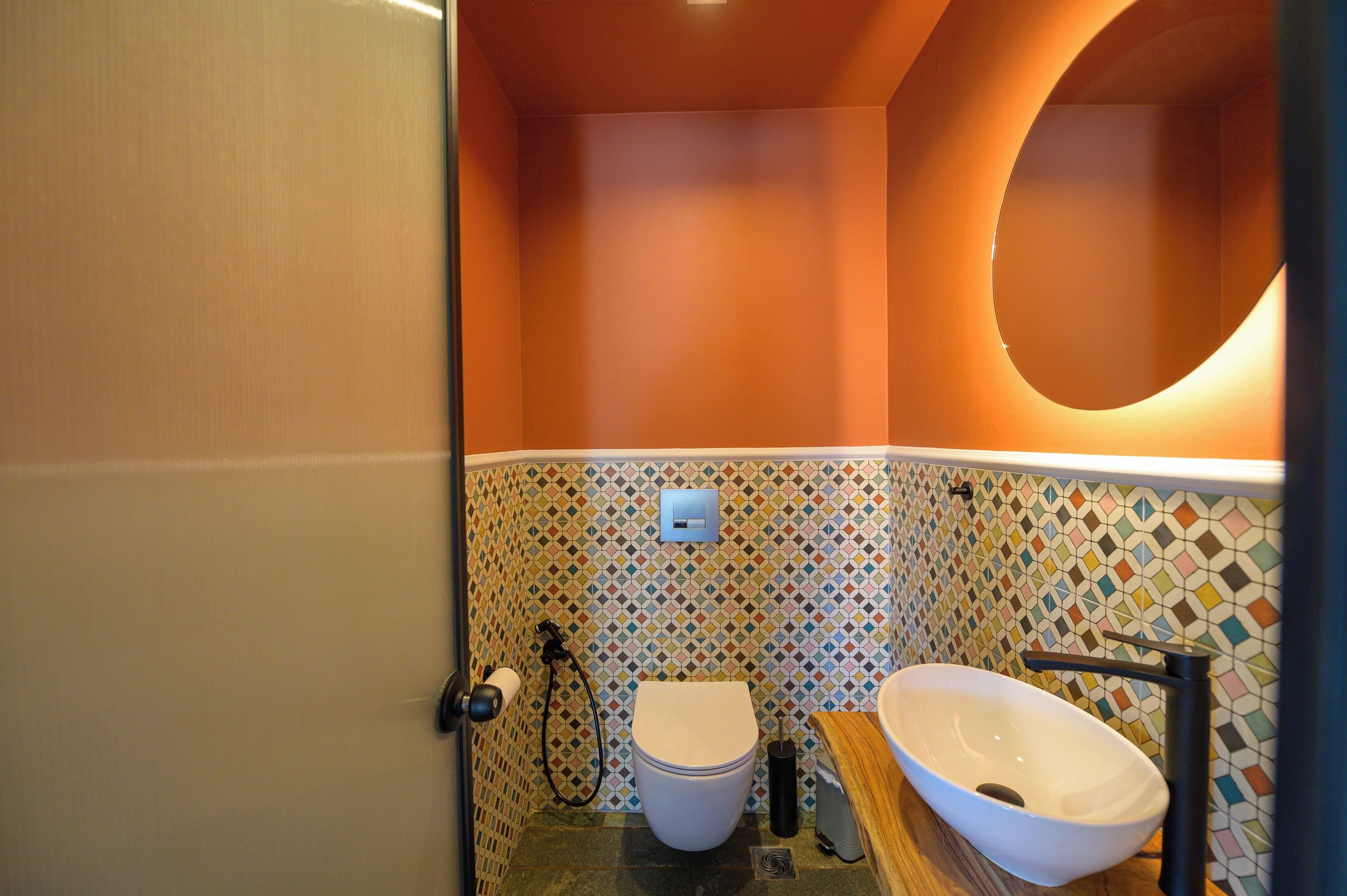 Een badkamer met een wit toilet, een wastafel op voet en een wand betegeld met kleurrijke mozaïek.
